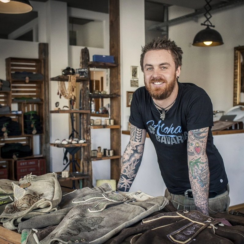 Man with tattoos standing behind a table with Bavarian leather trousers of Thalhammer Lederhosen